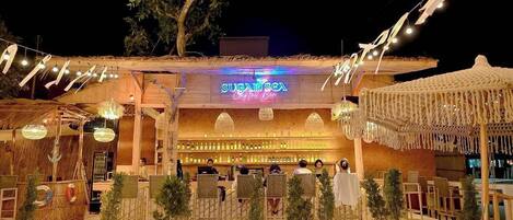 A cozy outdoor bar area with a neon sign reading "SUGAR SEA Bar" and a variety of seating arrangements.