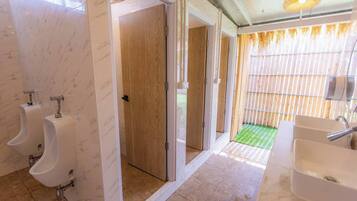 Une salle de bain moderne avec des murs en marbre, des portes en bois et un tapis vert menant à un espace extérieur.