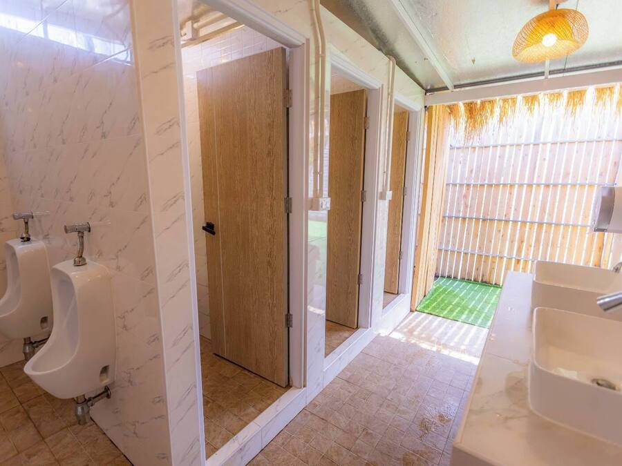 Une salle de bain moderne avec des murs en marbre, des portes en bois et un tapis vert menant à un espace extérieur.