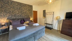 A modern bedroom with a large bed, a bedside table with a lamp, a hanging chair, and a TV on a dresser. - Das Lalelou- Familienurlaub Zentral in Braunlage mit Eigenem Garten (Braunlage)