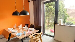 A dining area with a table set for four, a wooden chair, and a view of the outdoors through a large window. - Das Lalelou- Familienurlaub Zentral in Braunlage mit Eigenem Garten (Braunlage)