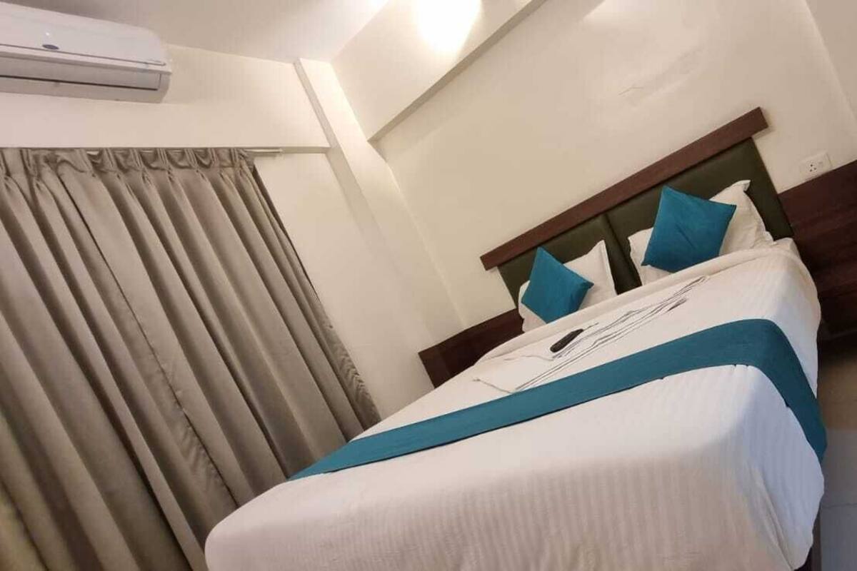 A hotel room with a bed, curtains, and an air conditioning unit.