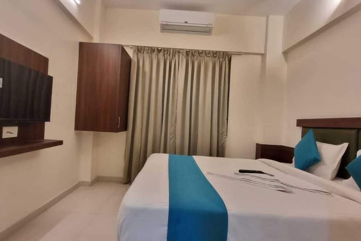 A hotel room with a bed, a TV mounted on the wall, a wardrobe, and a curtain.