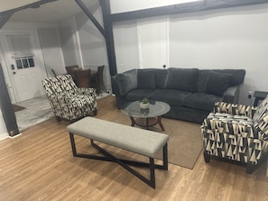 Uma sala de estar com um sofá modular cinza escuro, duas poltronas estampadas, uma mesa de centro redonda com uma planta e um banco cinza.