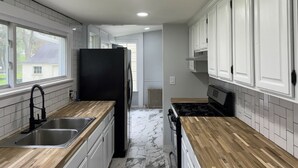 A kitchen with white cabinets, a black refrigerator, a stove, and a sink. - Serene Country Cottage (Woodbridge)