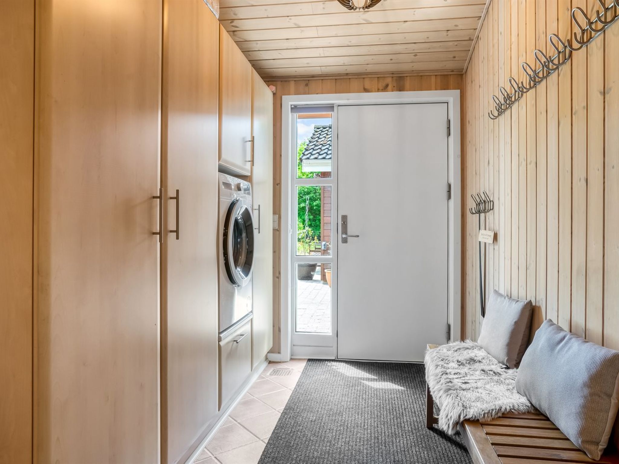 Lavandería con lavadora, puerta al exterior y un banco con almohadones.