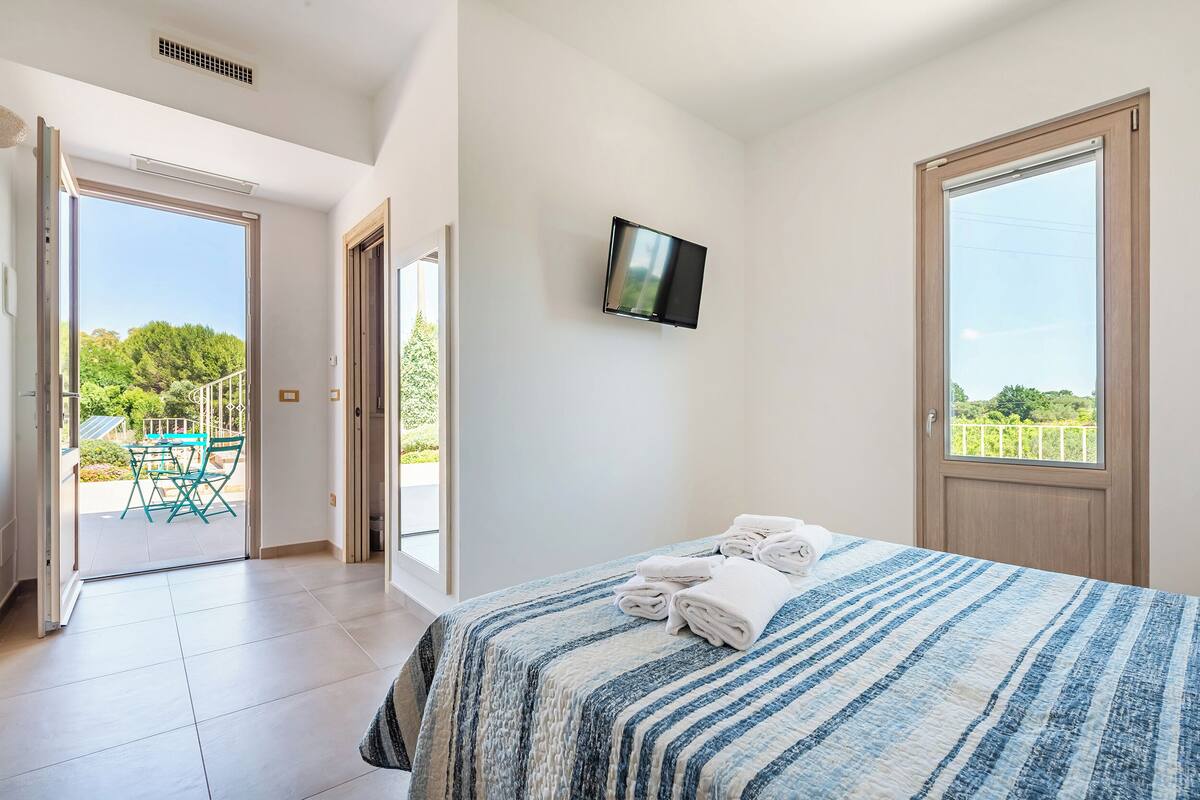 Une chambre à coucher avec un lit, une télévision et un balcon équipé d’une table et de chaises.