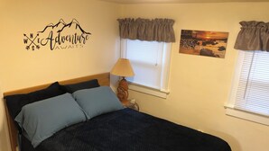 Une chambre à coucher avec un lit, une horloge murale et deux fenêtres avec des rideaux.