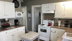Une cuisine avec des meubles blancs, une cuisinière, un four à micro-ondes et une petite table.