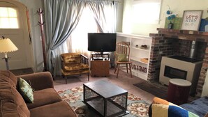 Un salon chaleureux avec un canapé marron, une chaise en bois, un téléviseur, une cheminée et un tapis à motifs.