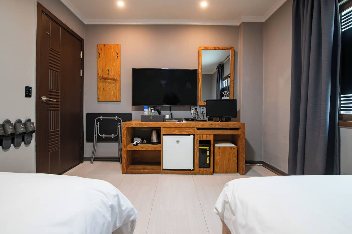 Une chambre d’hôtel avec deux lits, un bureau en bois avec une télévision, un petit réfrigérateur et un miroir.