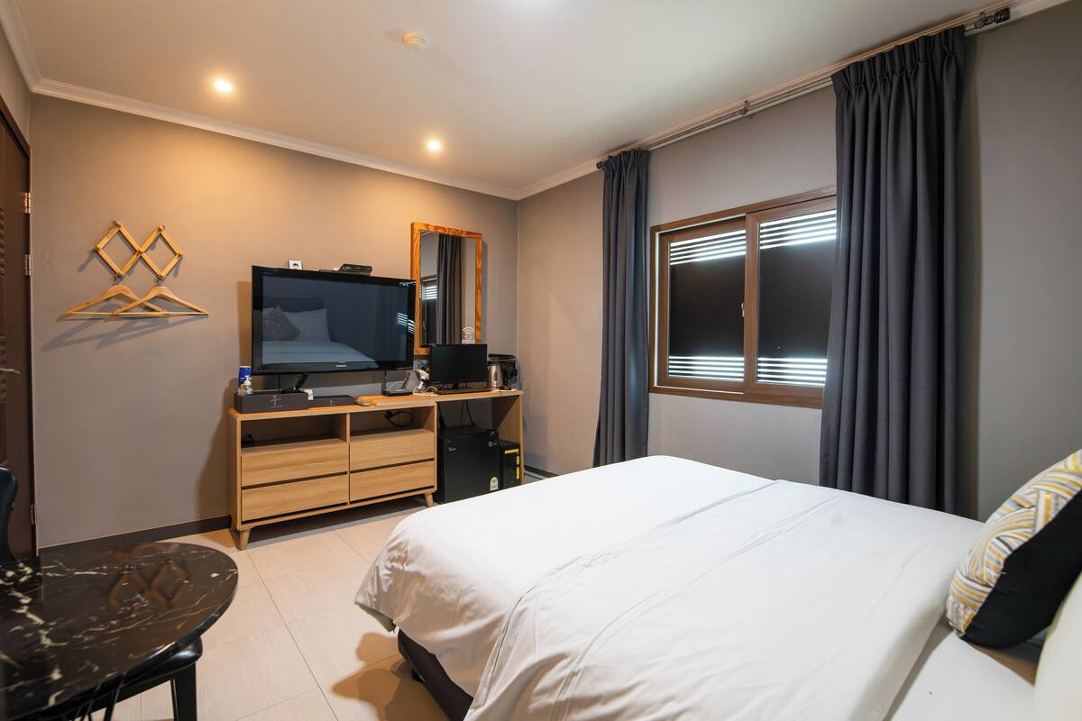 Une chambre d’hôtel avec un lit, une télévision, un bureau avec un ordinateur et une fenêtre avec des rideaux.
