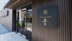 Entrada de un hotel de negocios con fachada moderna, puerta de cristal transparente y un cartel con el nombre y el logotipo del hotel.