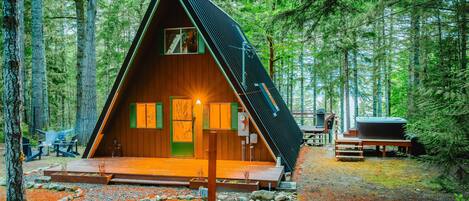 A wooden cabin with a sloped roof, surrounded by a forest.