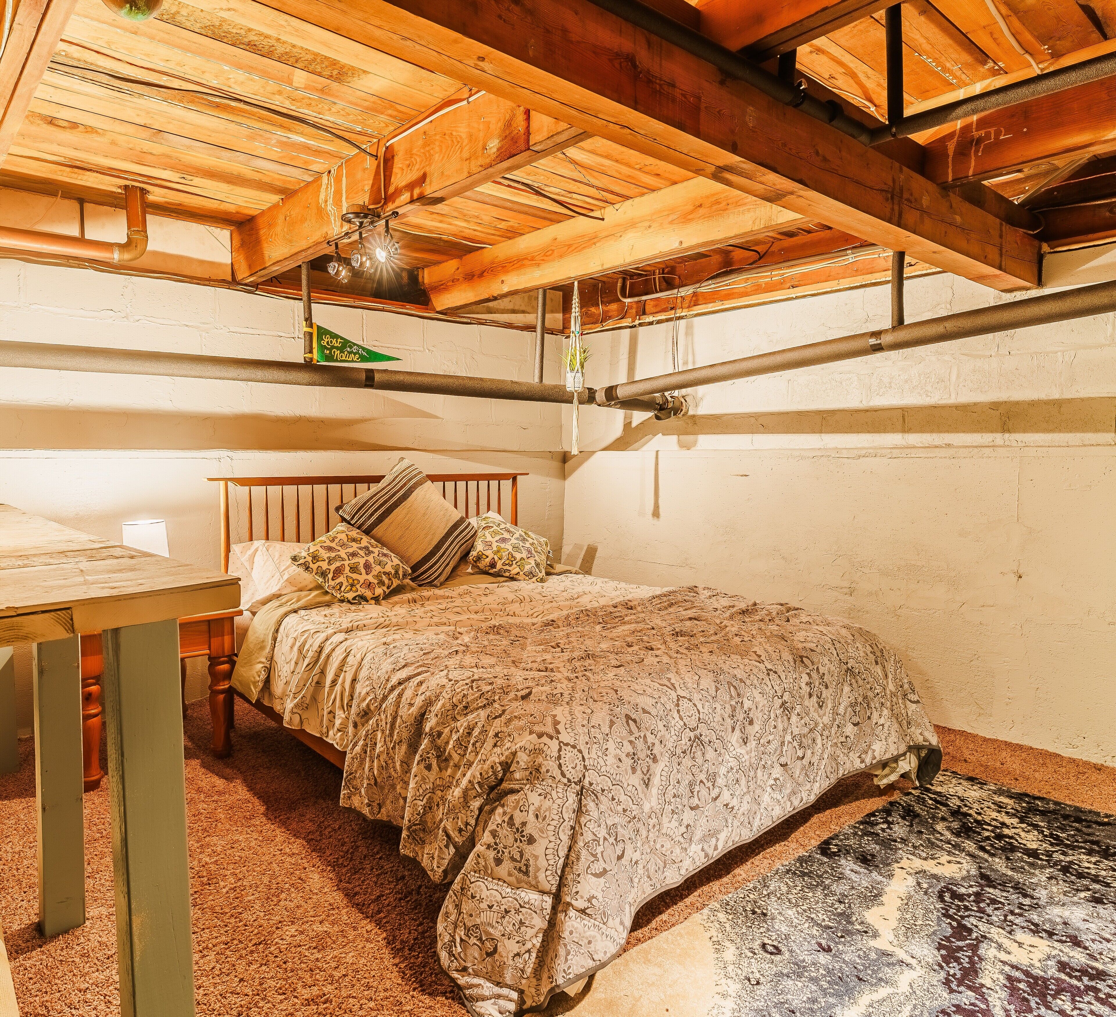 A cozy bedroom with a wooden ceiling, a bed with patterned bedding, and a small table with a lamp.