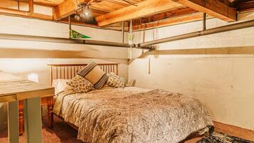 A cozy bedroom with a wooden ceiling, a bed with patterned bedding, and a small table with a lamp.