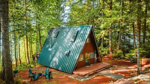 Une cabane avec un toit en pente, entourée d’une forêt.