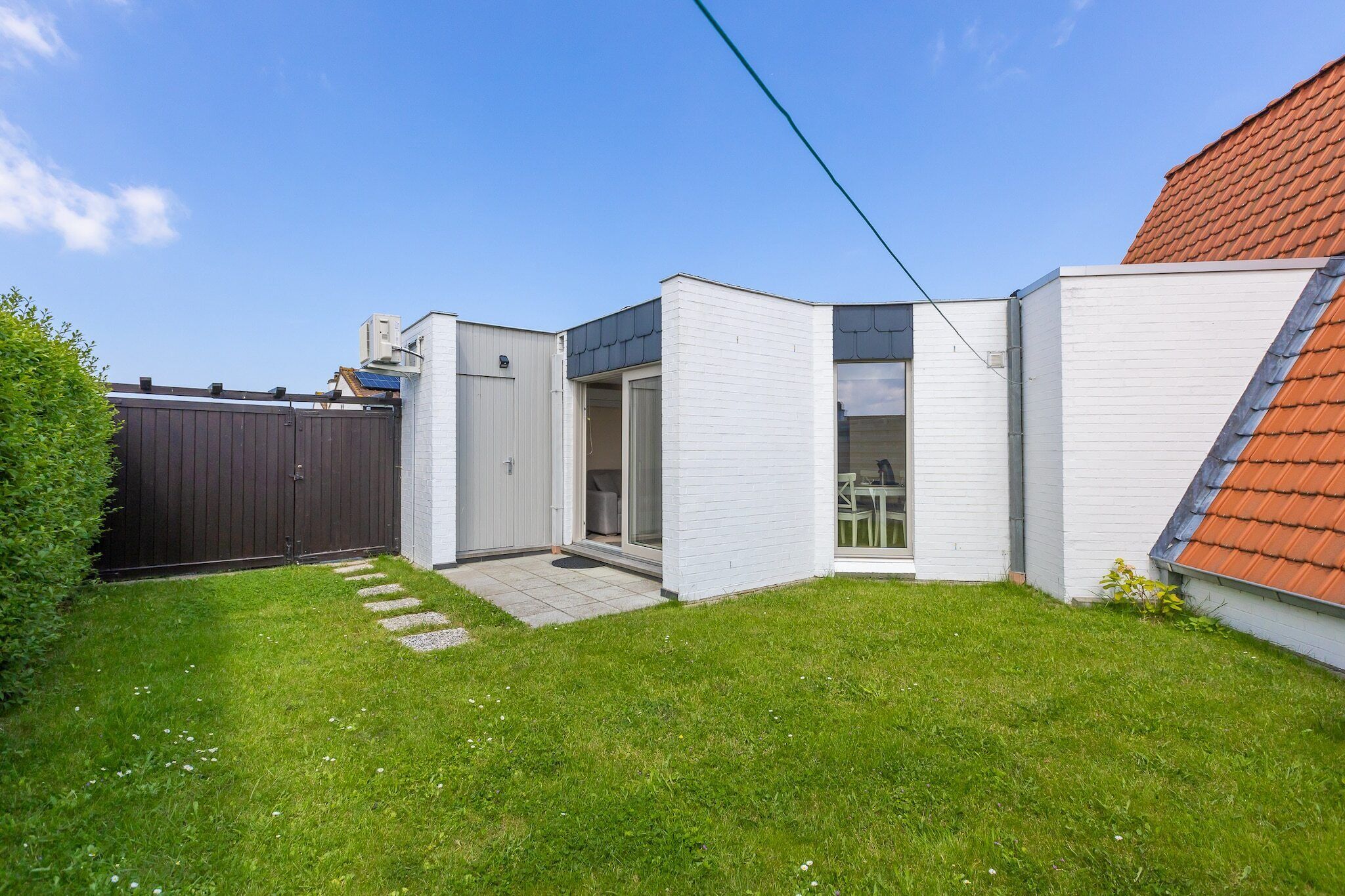 Een modern huis met een kleine tuin, een houten hek en een dak met rode tegels.