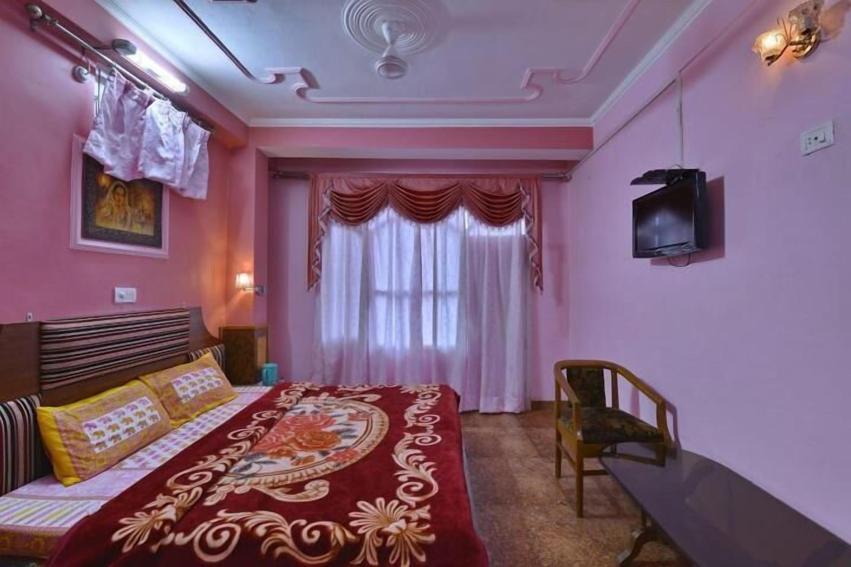 Une chambre à coucher avec un lit, une chaise, un téléviseur et une fenêtre avec des rideaux.