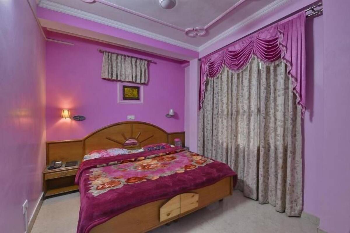 A bedroom with a wooden bed, a pink wall, a nightstand, a lamp, and curtains.