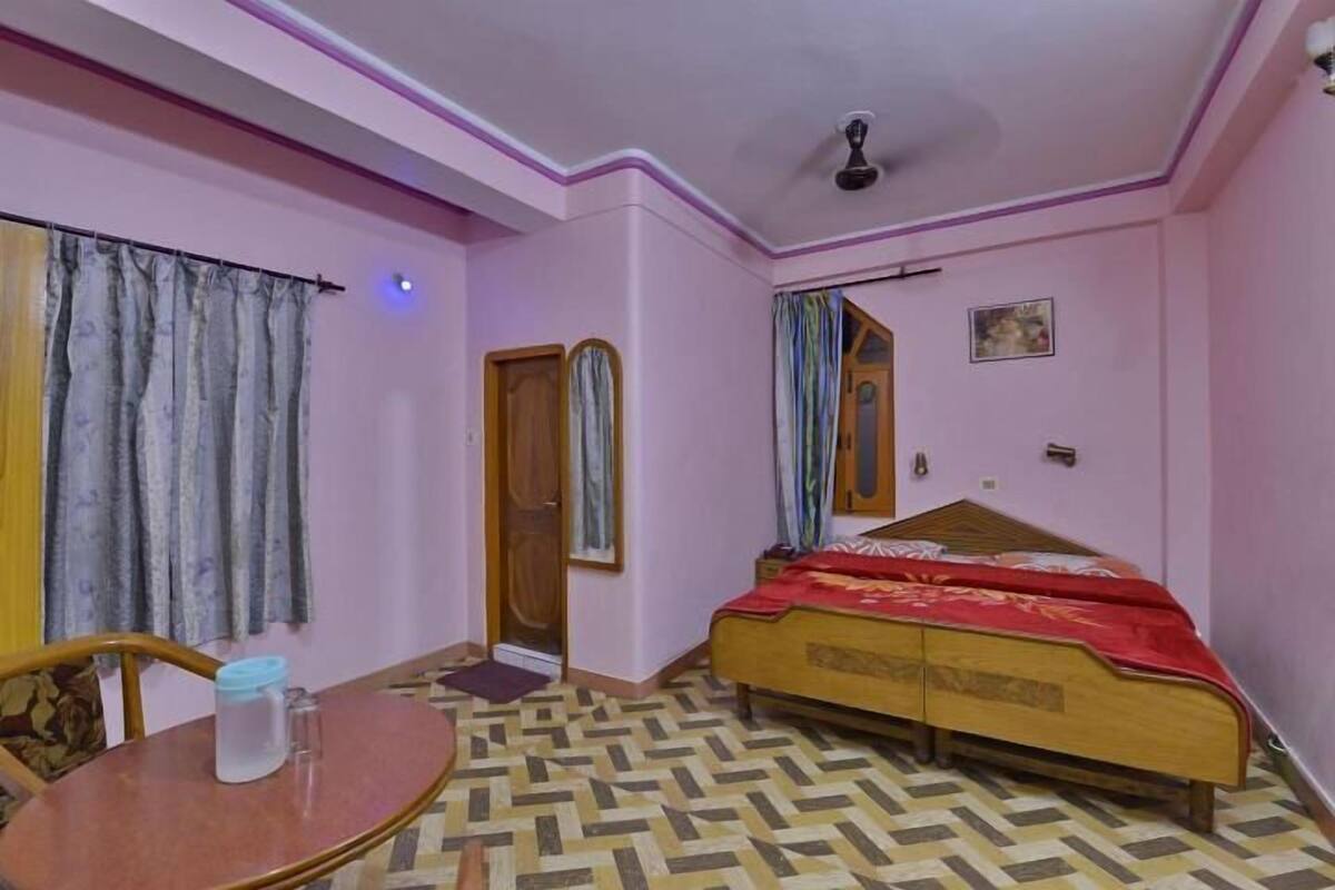 A bedroom with a bed, a wooden table, a chair, a ceiling fan, and a patterned floor.