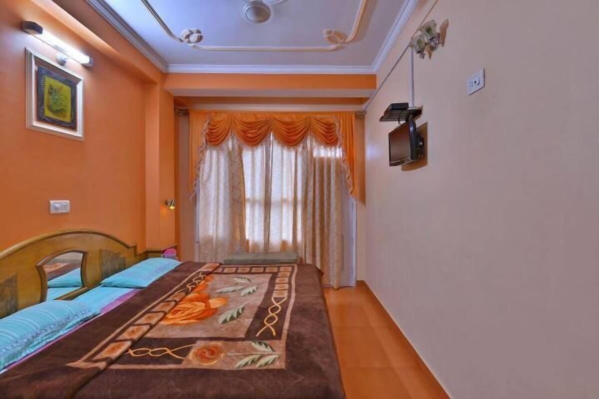 A bedroom with a bed, a nightstand, a wall-mounted TV, and a window with curtains.