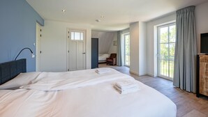 A spacious bedroom with a large bed, a chair, a television, and a balcony with curtains.