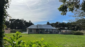 A building with a sloped roof and large windows, surrounded by a grassy area and trees.