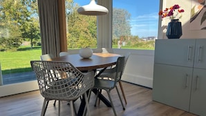 A dining area with a round table, two chairs, a vase with flowers, and a view of the outdoors.
