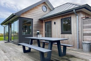 Un espace de restauration extérieur moderne, doté d’une terrasse en bois, d’une table en métal et de bancs.