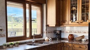 Una cocina con armarios de madera, encimera de granito, ventana con vista a un campo y una cafetera.