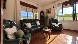 Una sala de estar con un sofá de cuero, una mesa de centro de madera y vistas a un paisaje verde a través de amplios ventanales.