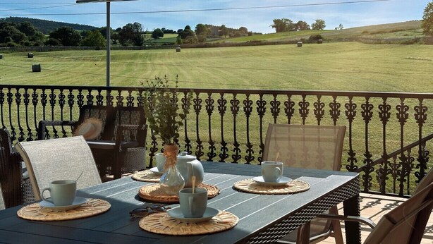 Un patio con una mesa lista para dos, sillas de exterior y vistas a un campo cubierto de césped.
