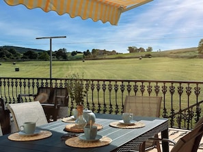 A patio with a table set for two, outdoor chairs, and a view of a grassy field.
