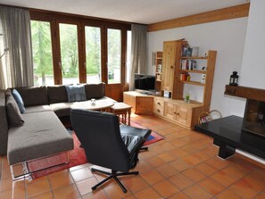 Una sala de estar con sofá, sillón, televisor, una estantería con libros y chimenea.