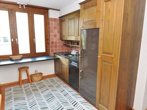 A compact kitchen with wooden cabinets, a stainless steel refrigerator, and a tiled backsplash.