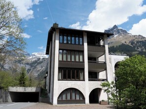 A modern building with a balcony, arched windows, and a mountain backdrop.