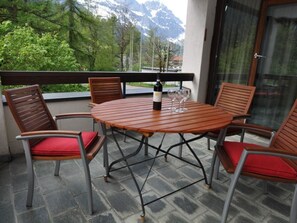 A round table with chairs on a balcony, a bottle of wine, and a glass.