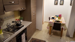 A kitchen with a stove, kettle, and cabinets. There is a dining table with chairs and a rug. - 1 bedroom apartment in florence (Firenze)