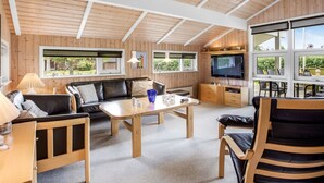 Un vaste espace de vie doté d’un plafond en bois, d’un grand téléviseur et d’une table à manger.