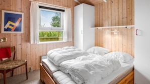 Une chambre avec un plancher en bois, un lit avec une literie blanche, une chaise, une fenêtre avec des rideaux et un luminaire au plafond.