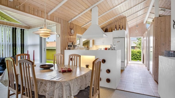 Une cuisine moderne avec des meubles en bois et un îlot central, un coin repas avec une table ronde et des chaises, et une vue sur l’extérieur.