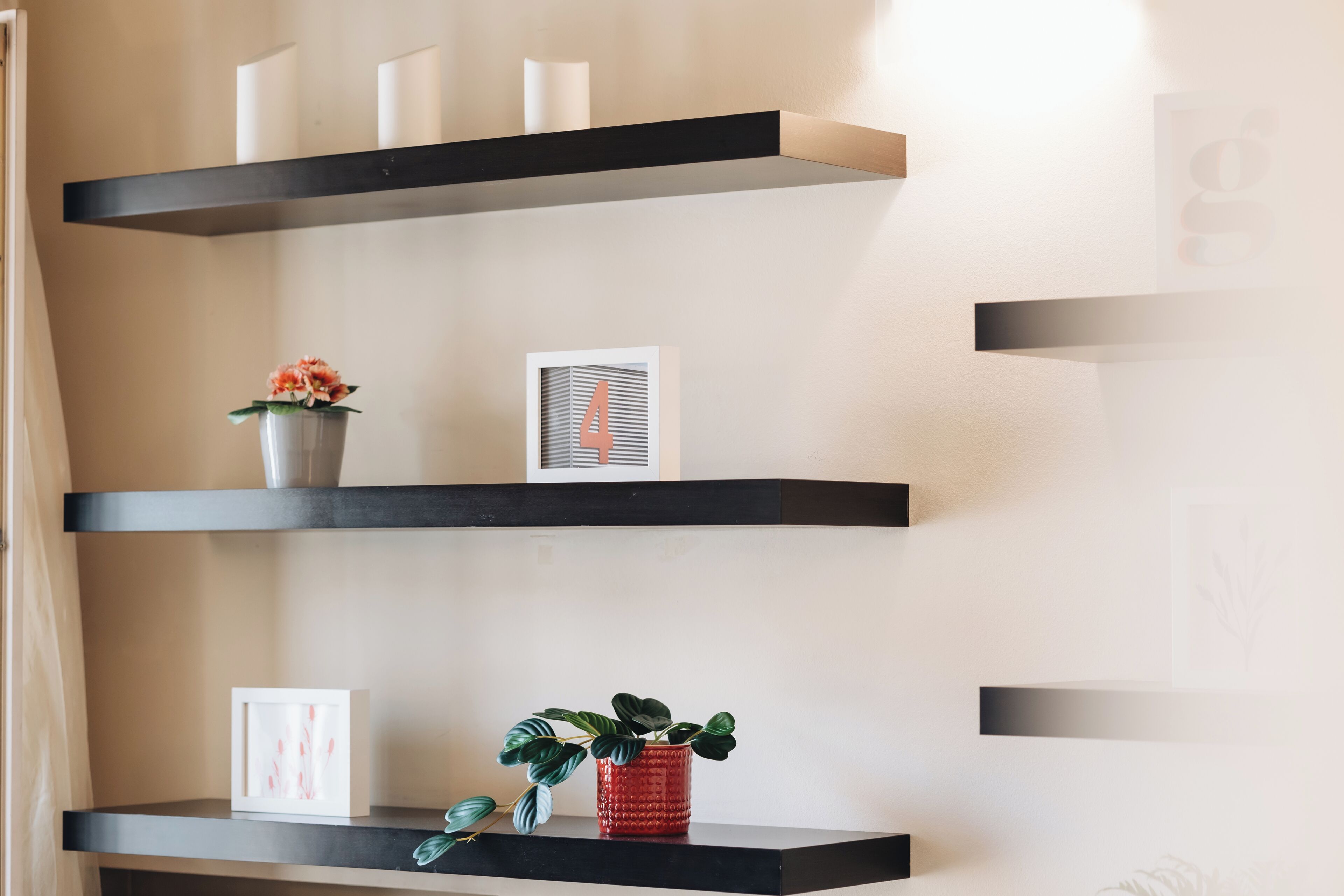 Een modern interieur met drie zwarte zwevende planken, elk versierd met decoratieve items zoals een potplant, ingelijste foto's en kaarsen.