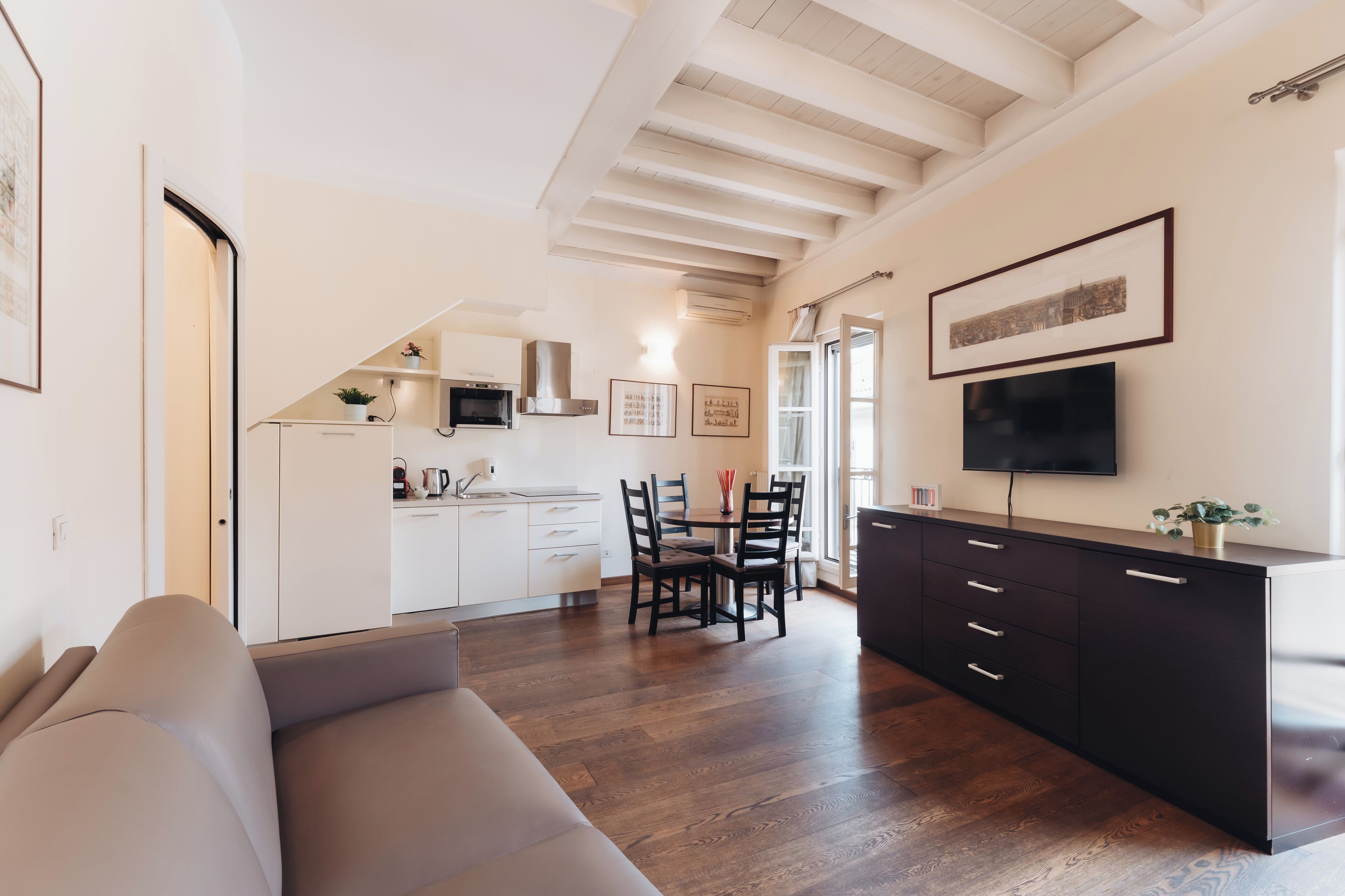 Ein modernes Wohnzimmer mit einer Couch, einem Essbereich mit Stühlen und einem Tisch, einer Küche mit Schränken und einem Herd sowie einem an der Wand montierten Fernseher.