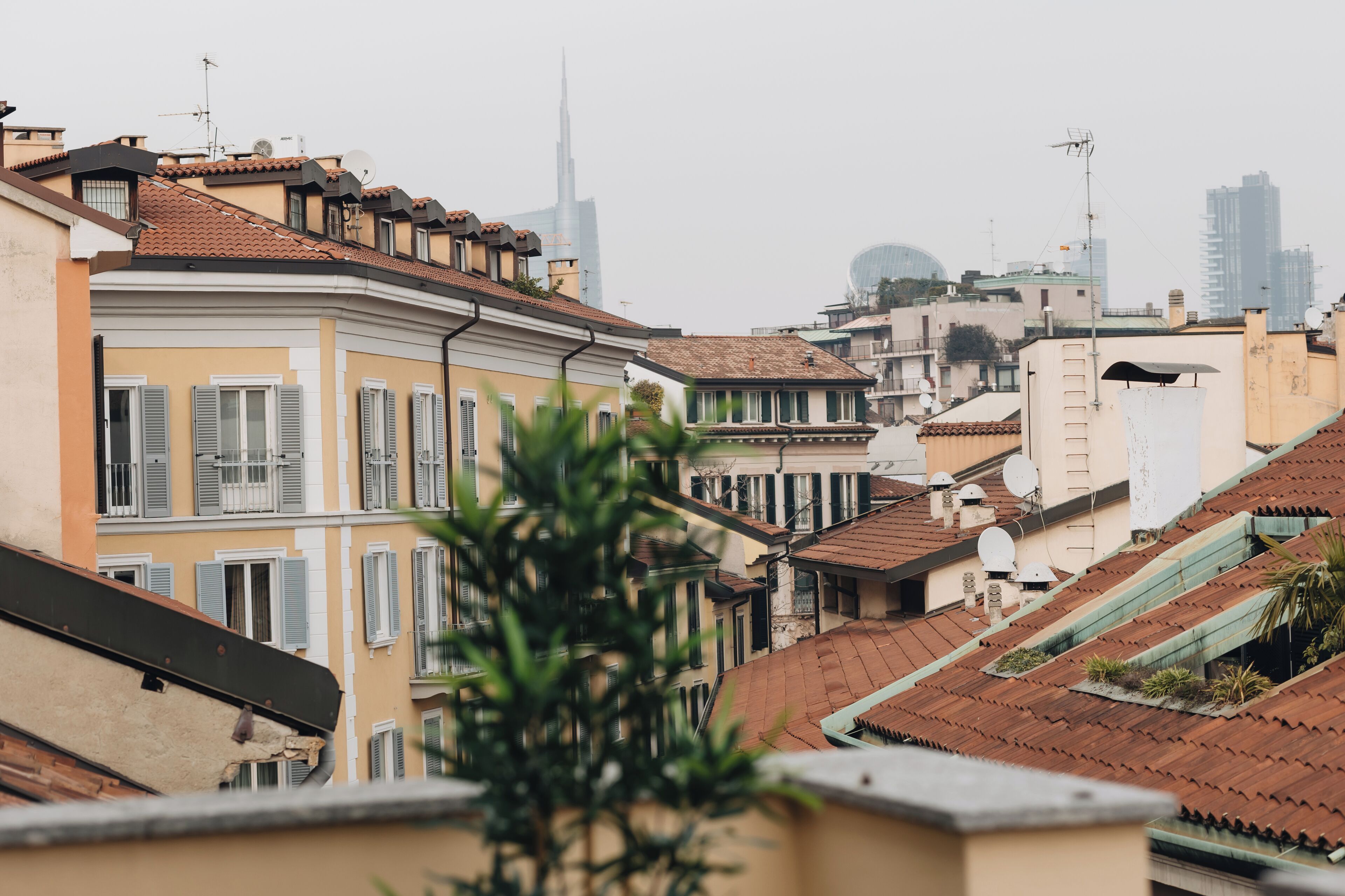 A row of traditional European buildings with terracotta roofs and balconies, overlooking a cityscape with modern skyscrapers.