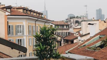 A row of traditional European buildings with terracotta roofs and balconies, overlooking a cityscape with modern skyscrapers.