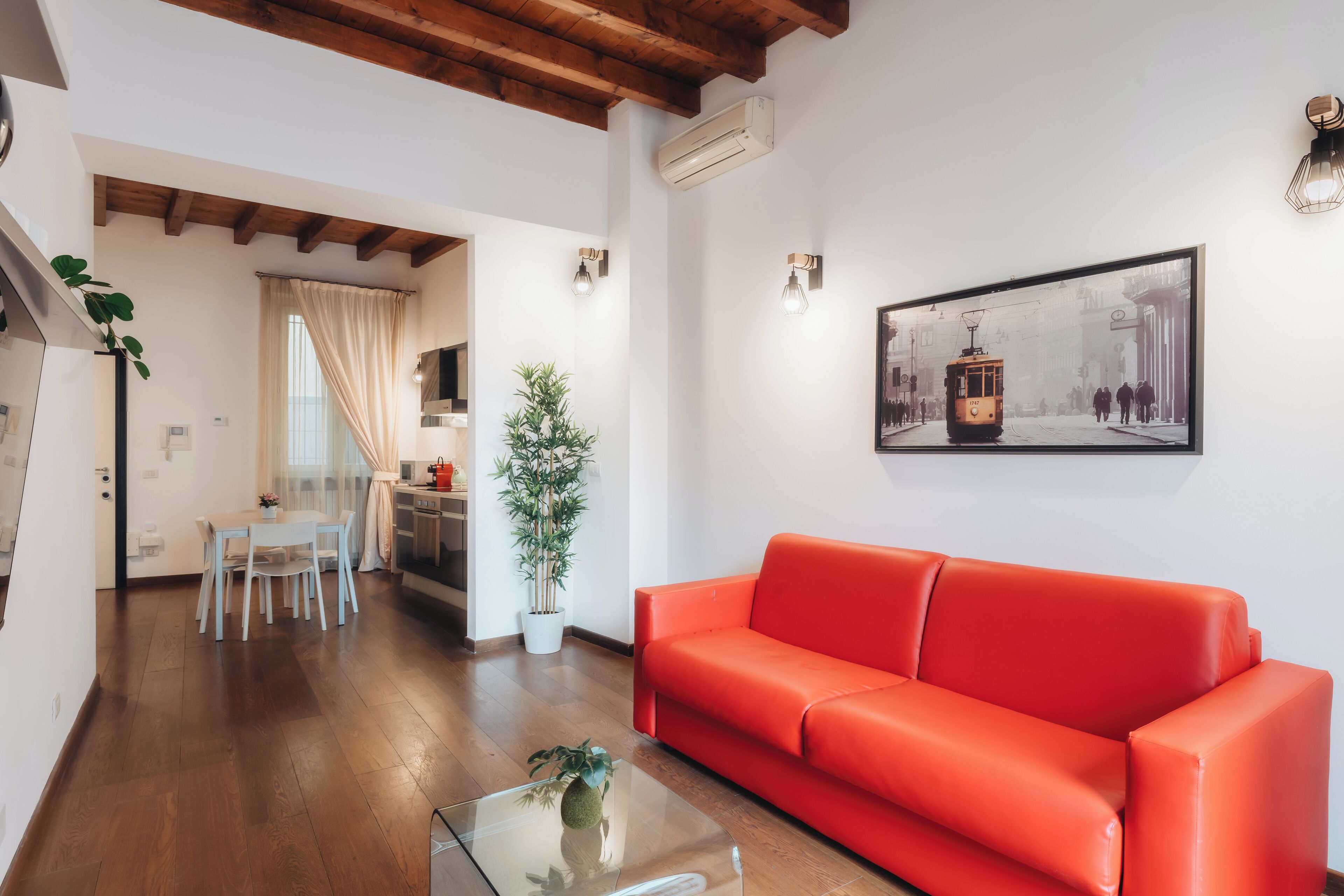 A modern living room with a red sofa, a glass coffee table, and a dining area with a white table and chairs.