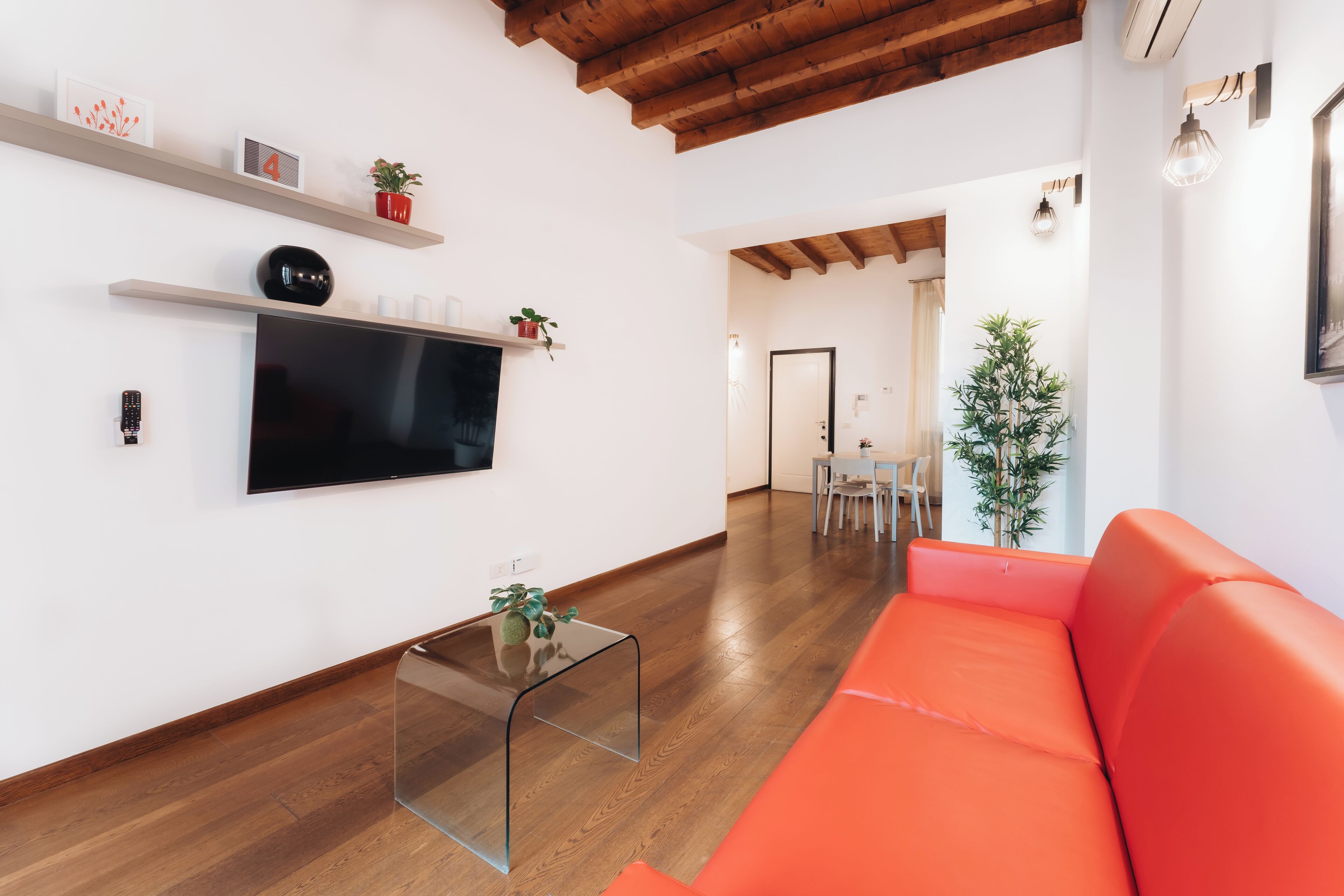 Un salon moderne avec un plancher en bois, un grand canapé orange, une table basse en verre et un téléviseur à écran plat fixé au mur.