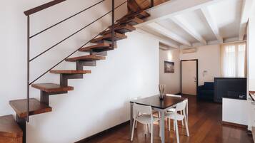 A modern interior with a wooden staircase, a dining area with white chairs, and a living space with a sofa and a TV.