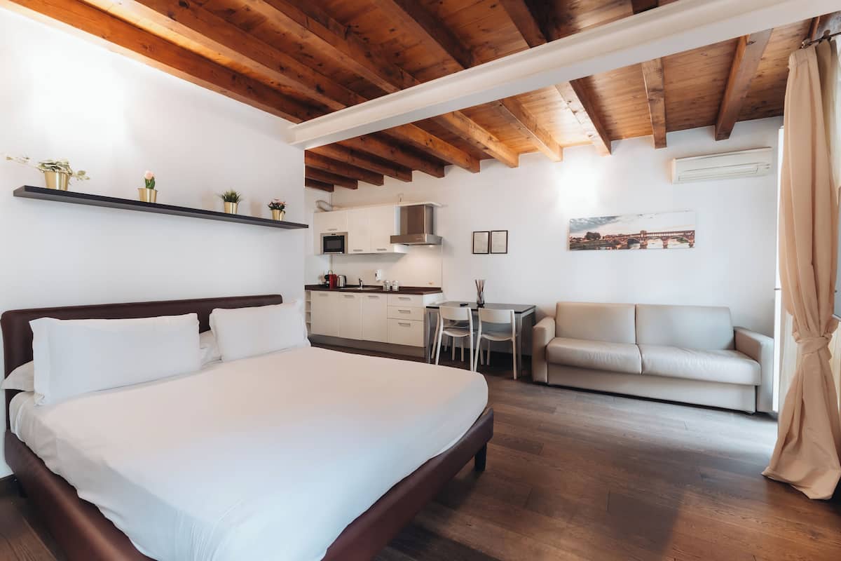 A bedroom with a large bed, a sofa, a desk, and a kitchenette.